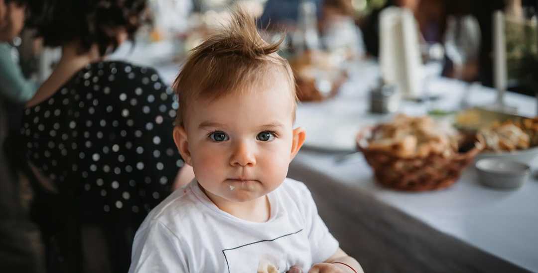 Baby sitting at a table with food in hands