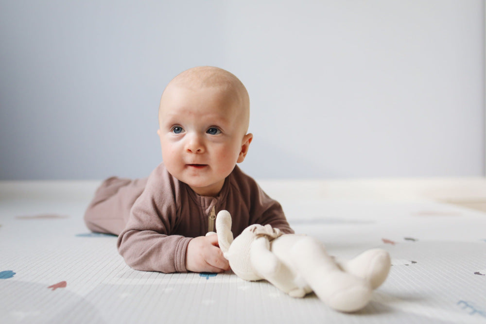 A baby lying on a flat surface with a toy