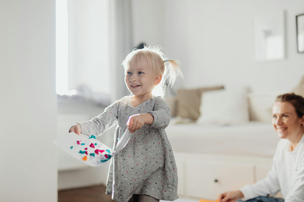 A toddler carrying her craft as her mom smiles